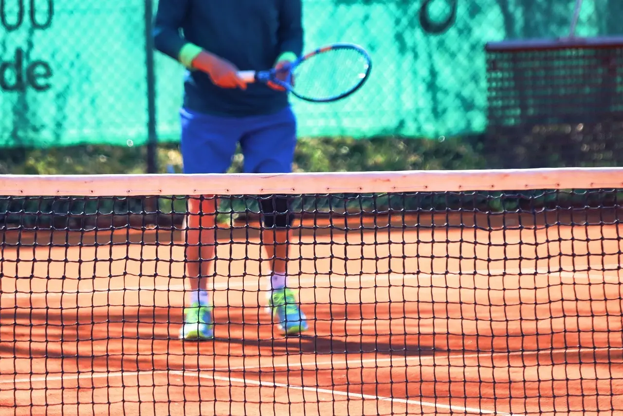Tennisspiller bag net på grusbane